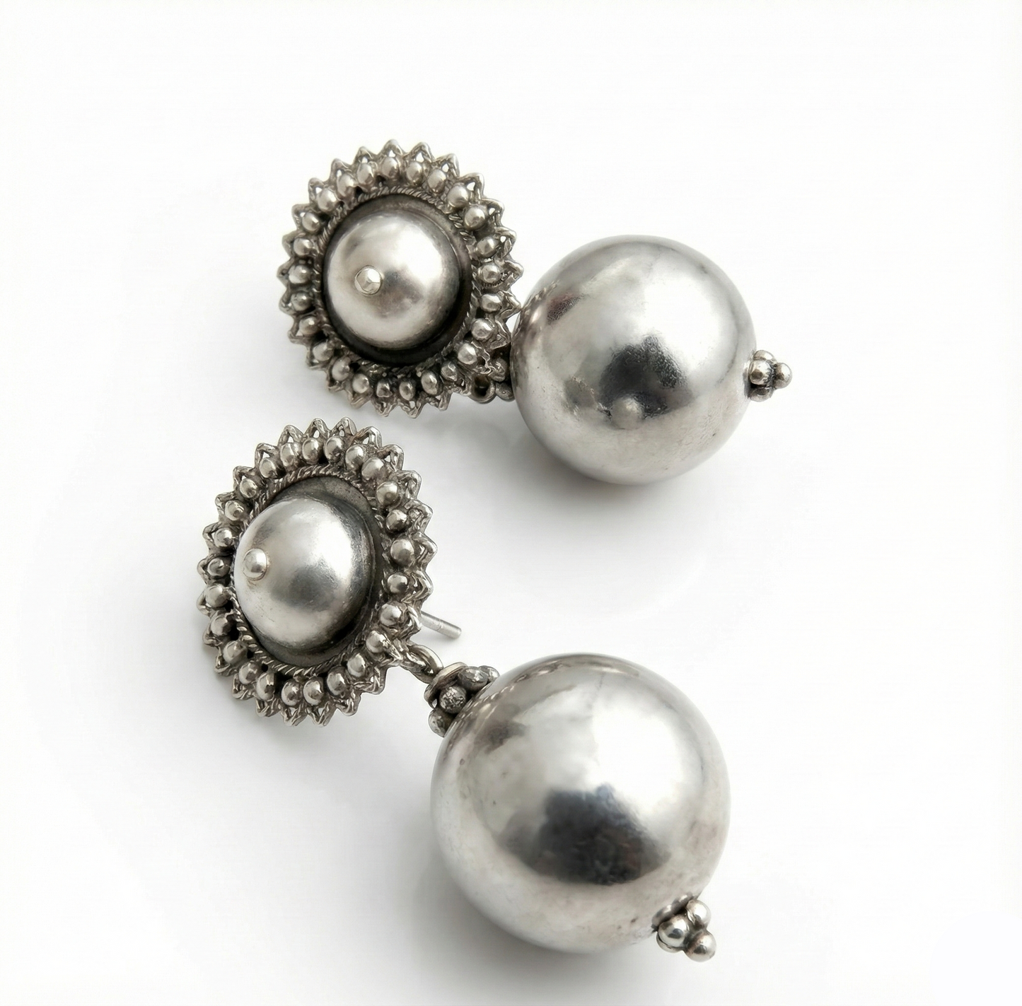 Pair of silver earrings with spherical and floral designs on a white background