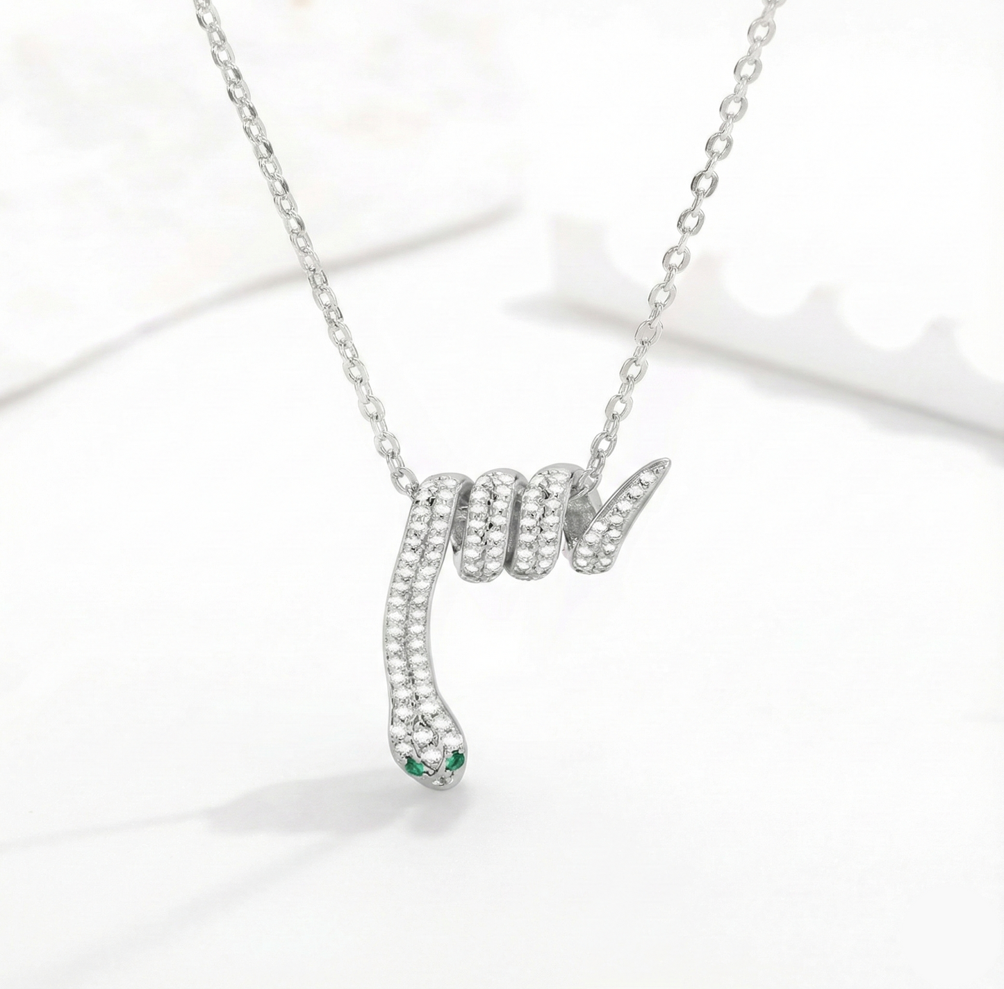 Silver snake-shaped pendant necklace with green gemstone on a white background