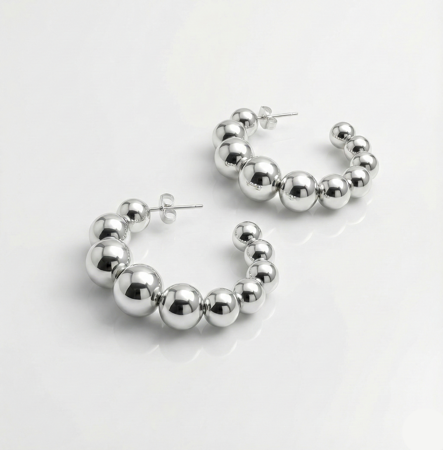 Silver hoop earrings with spherical beads on a white background