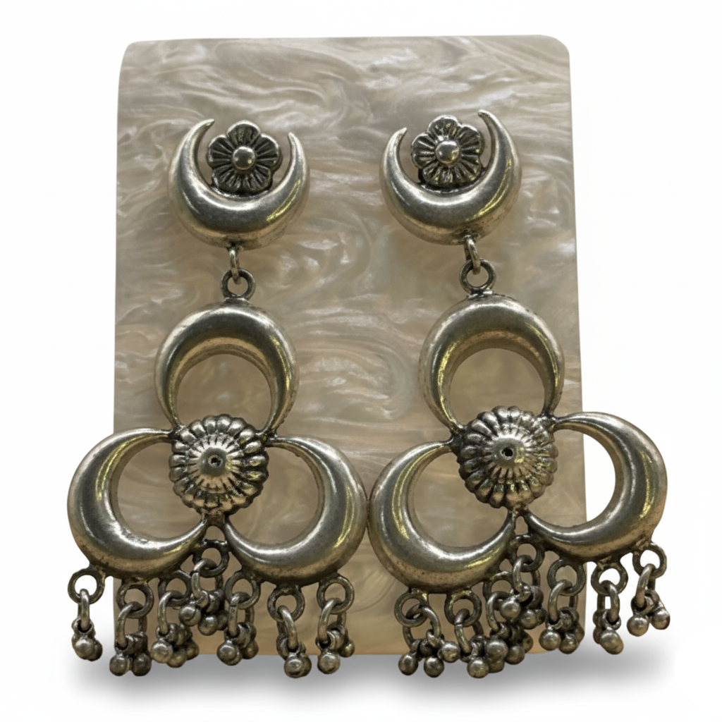 Pair of silver earrings with floral and crescent designs on a textured card.