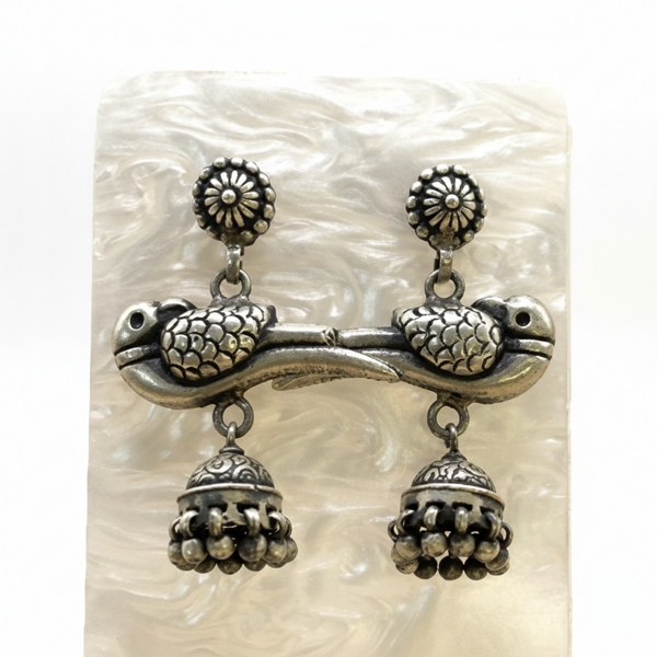 Pair of silver turtle earrings with jhumka designs on a textured white background