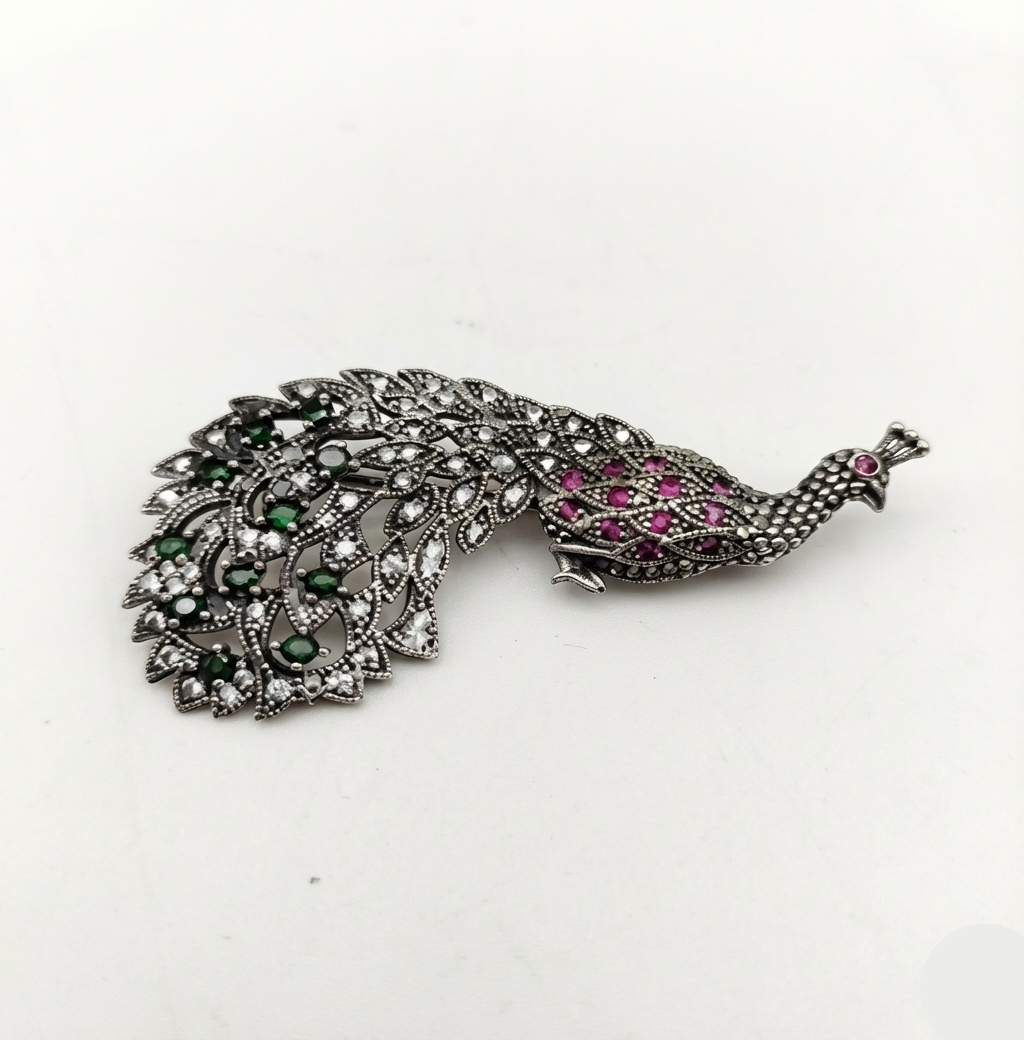 Peacock-shaped brooch with gemstones on a white background