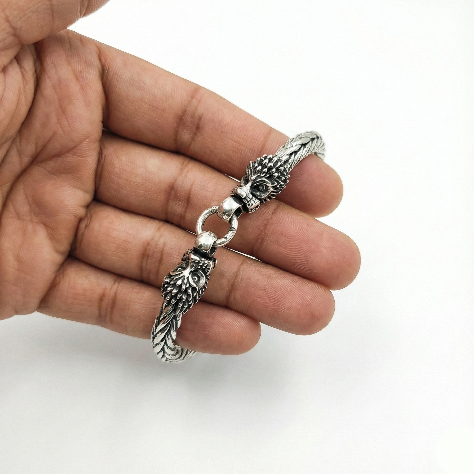 Silver pendant with leaf-like designs held in a hand against a white background