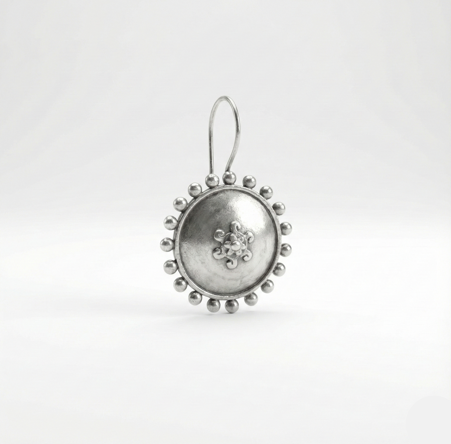 Silver earring with intricate design on a white background