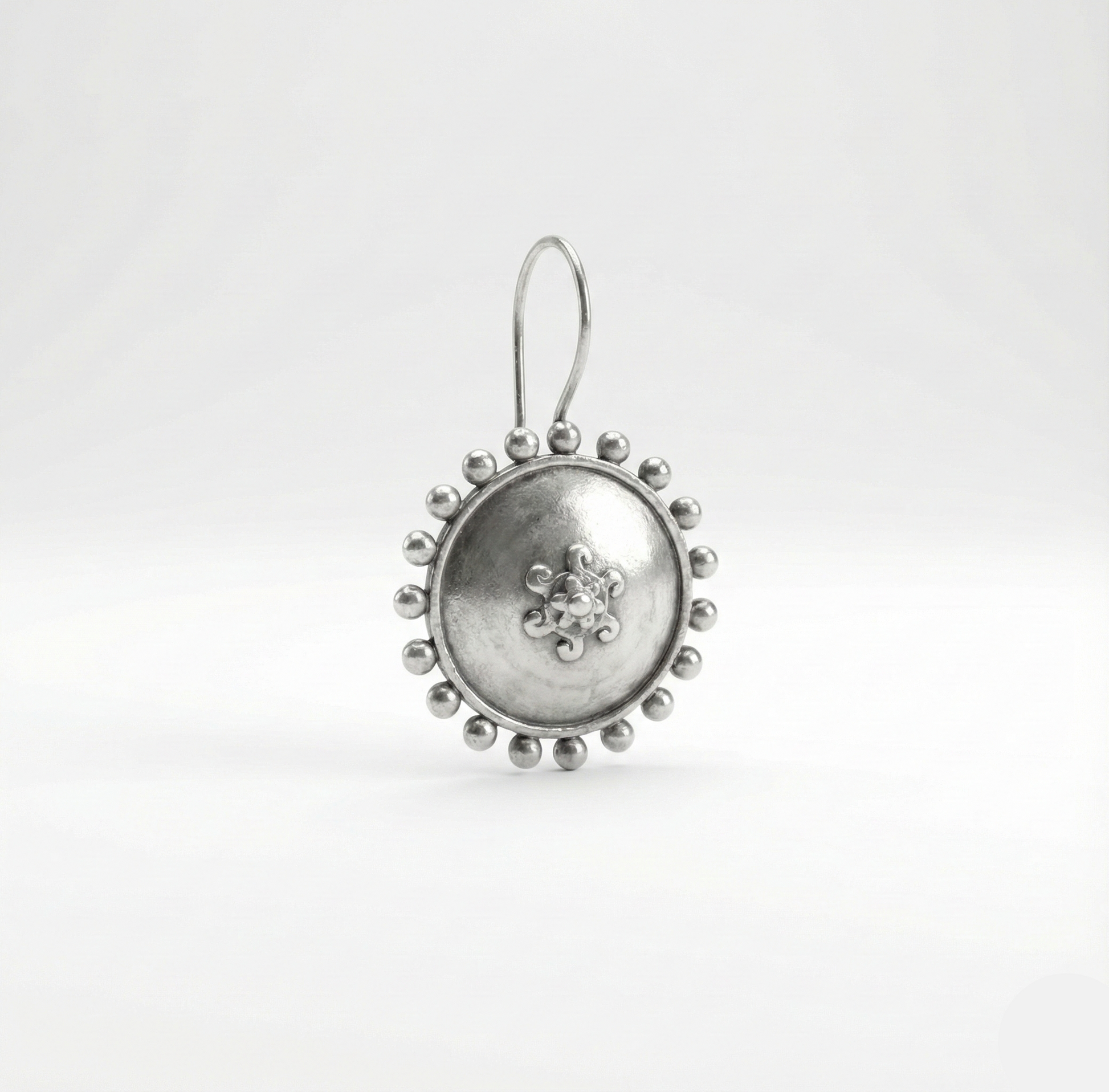 Silver earring with intricate design on a white background