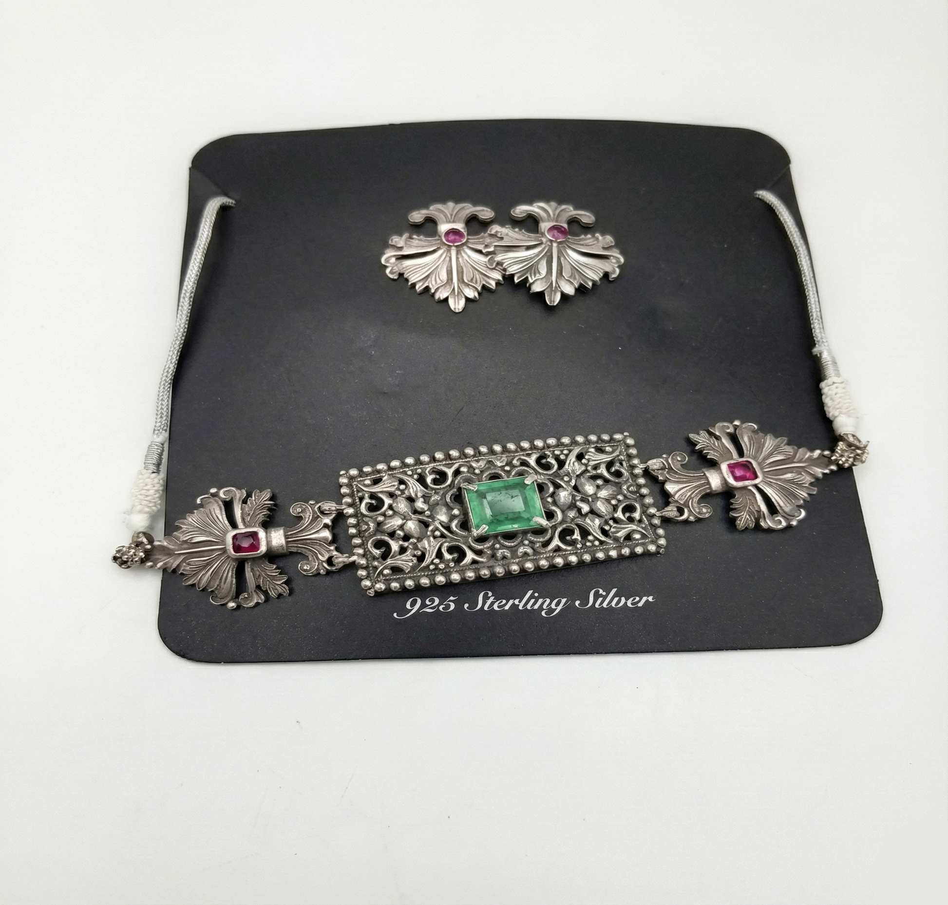 Silver jewelry set with emerald and rubies on a black card, on a white background
