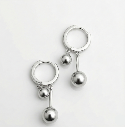 Pair of silver hoop earrings with dangling spherical charms on a light gray background