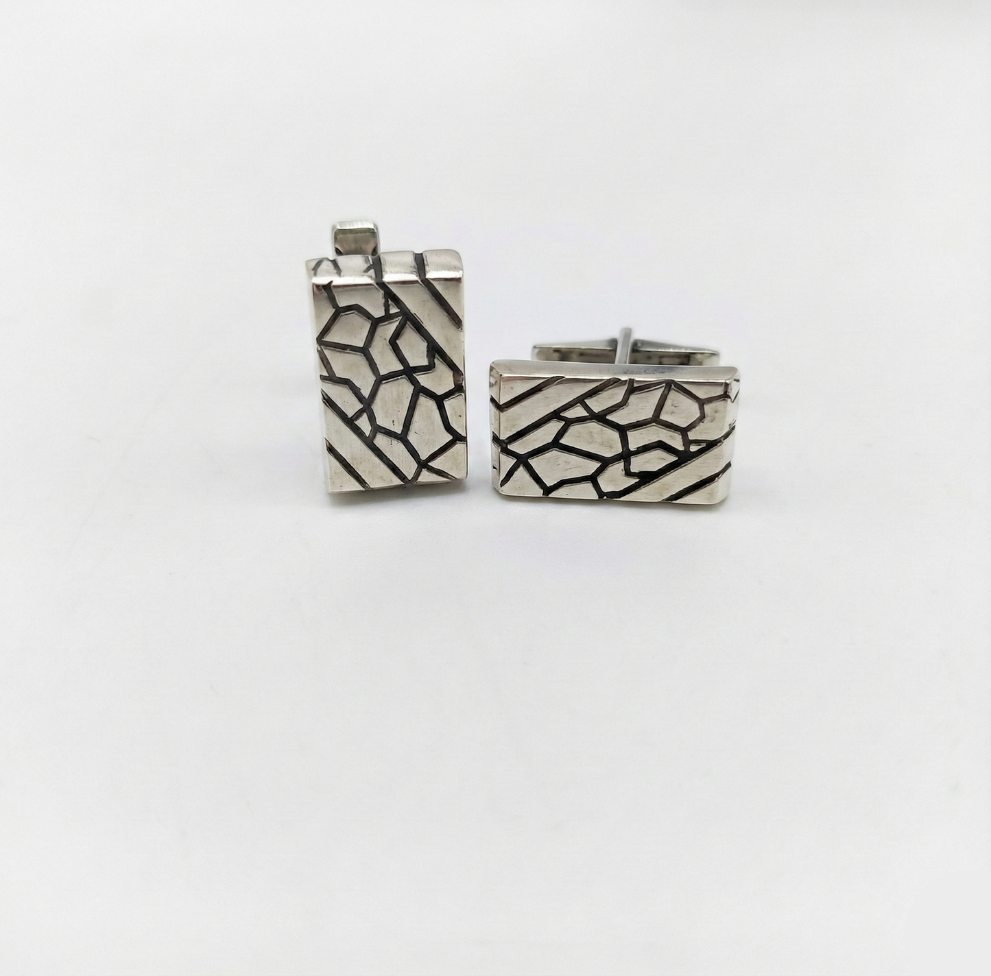 Pair of silver cufflinks with geometric pattern on a white background