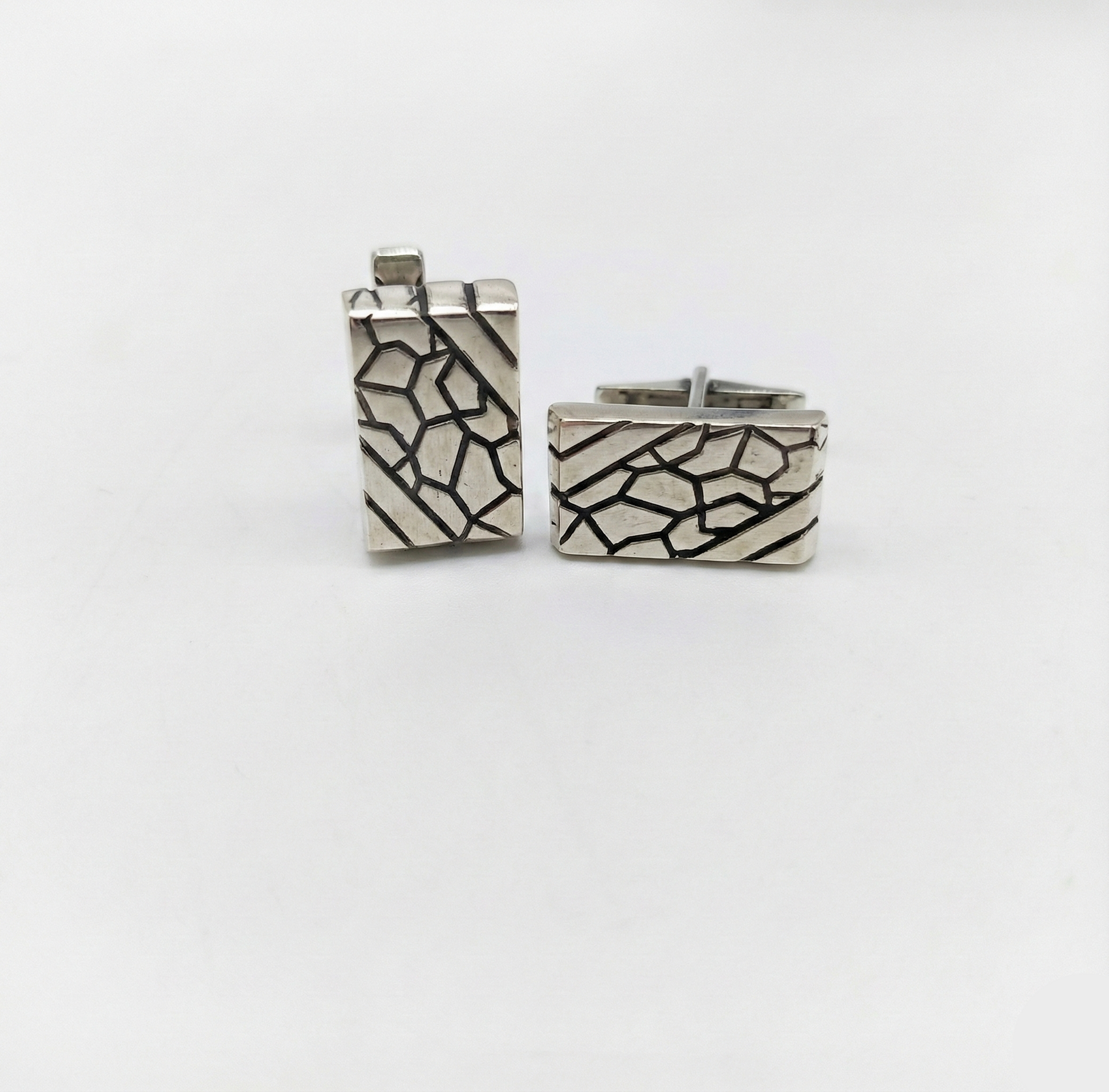 Pair of silver cufflinks with geometric pattern on a white background