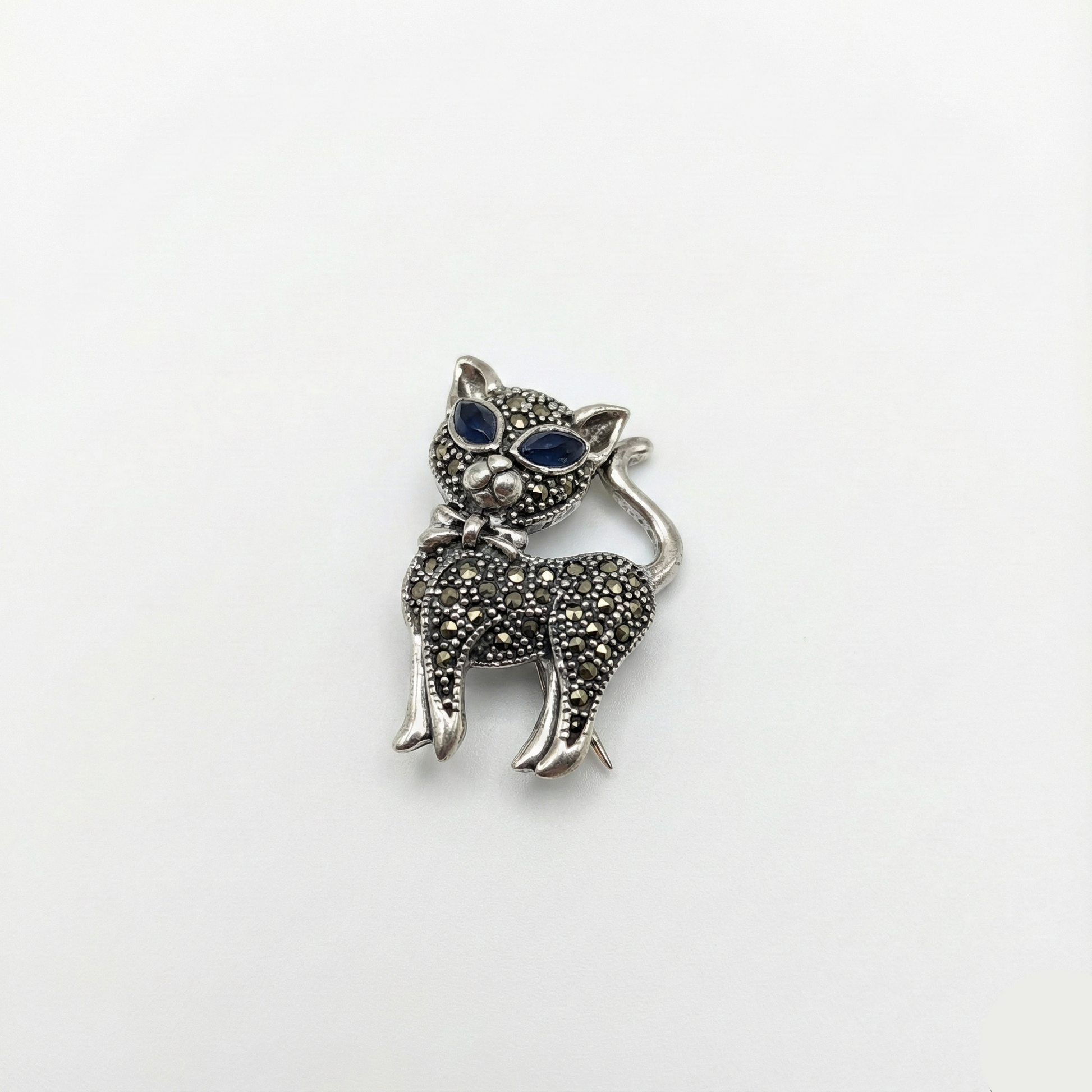 Silver cat-shaped brooch with blue gemstones on a white background