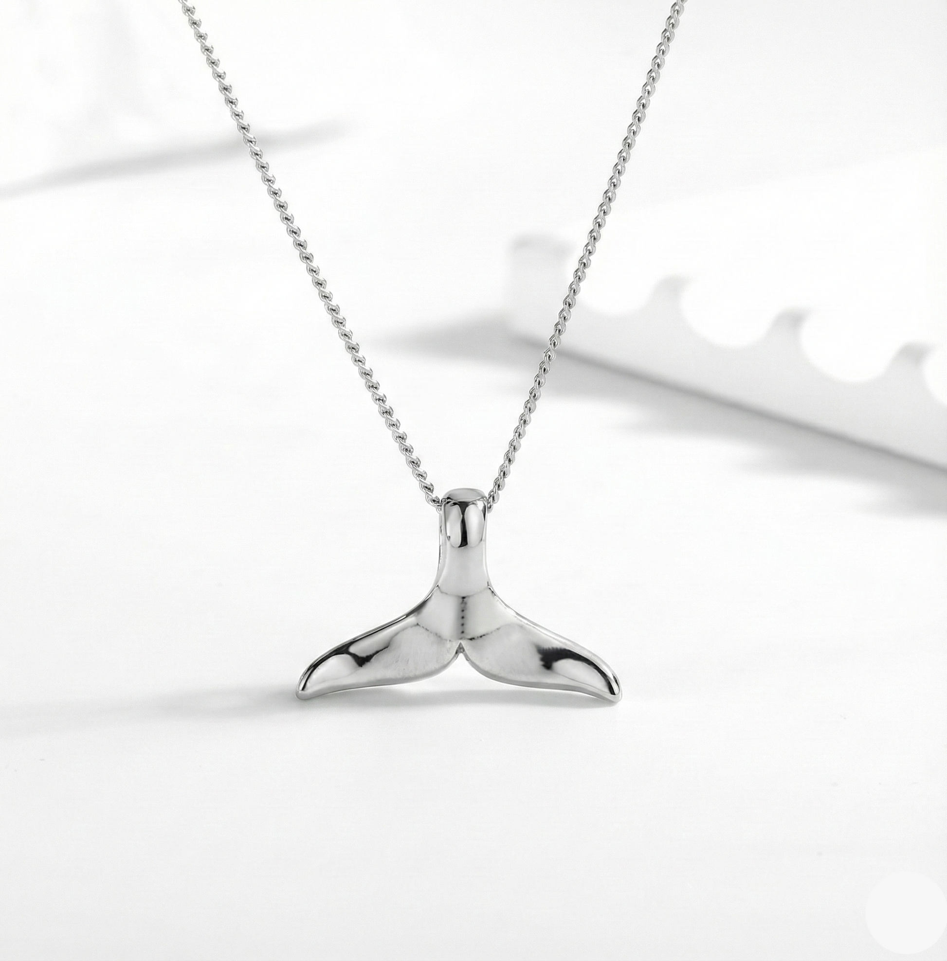 Silver whale tail necklace on a white background