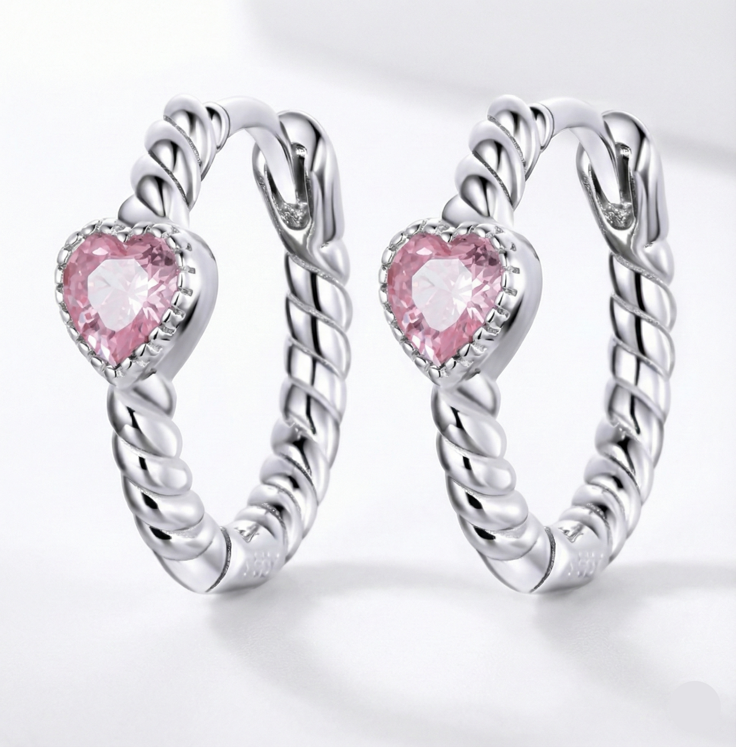 Silver hoop earrings with pink heart-shaped gemstones on a white background