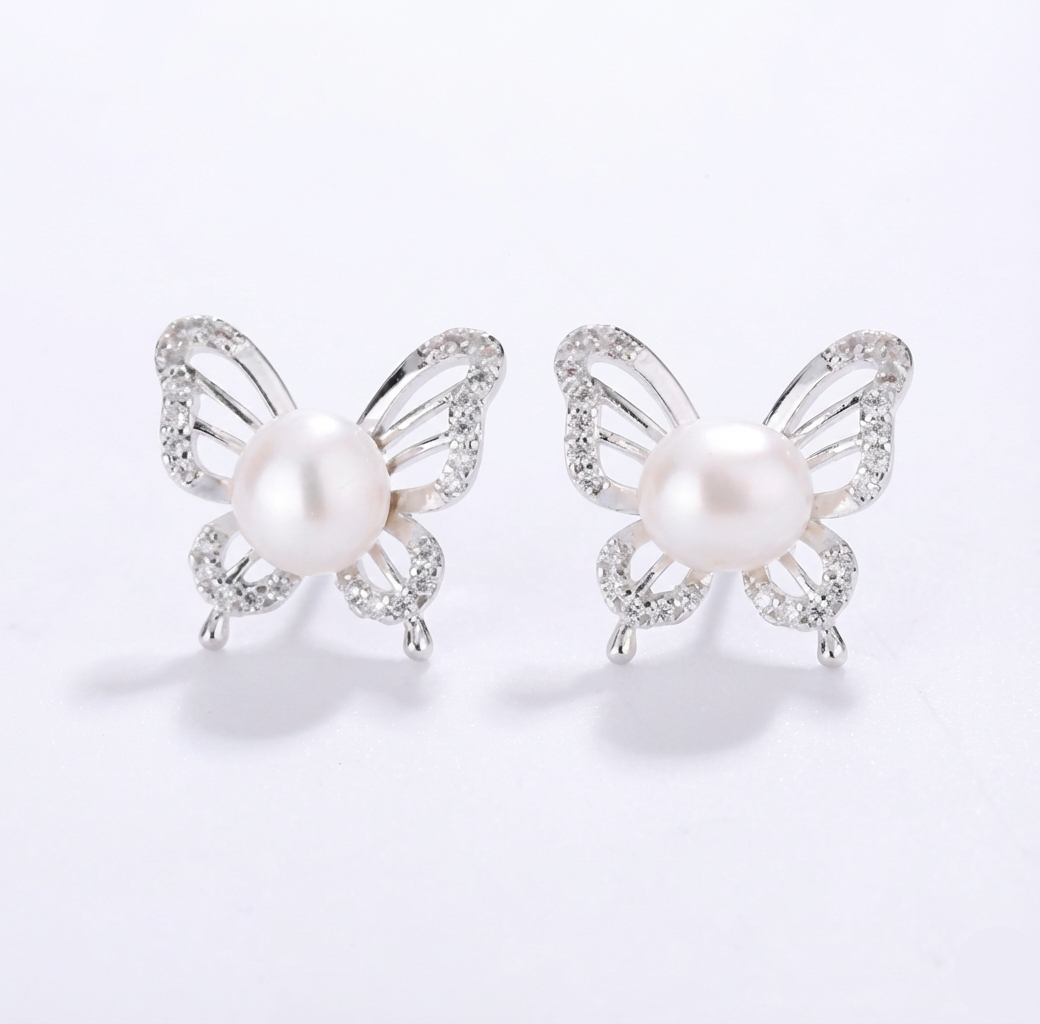 Butterfly-shaped earrings with pearl centers on a light gray background