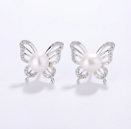 Butterfly-shaped earrings with pearl centers on a light gray background
