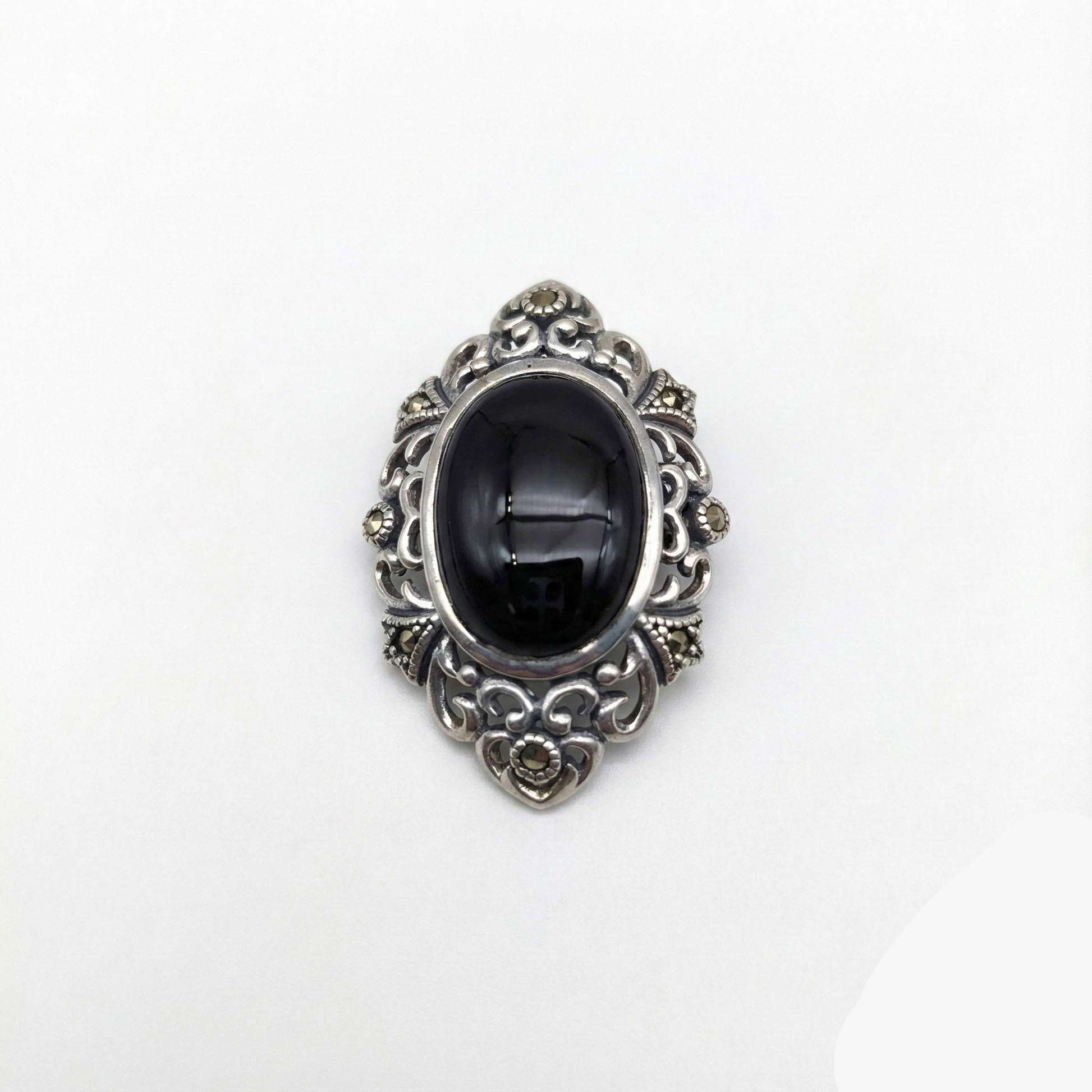 Decorative brooch with black center and silver intricate design on a white background