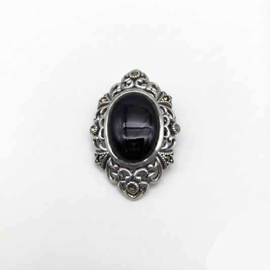 Decorative brooch with black center and silver intricate design on a white background