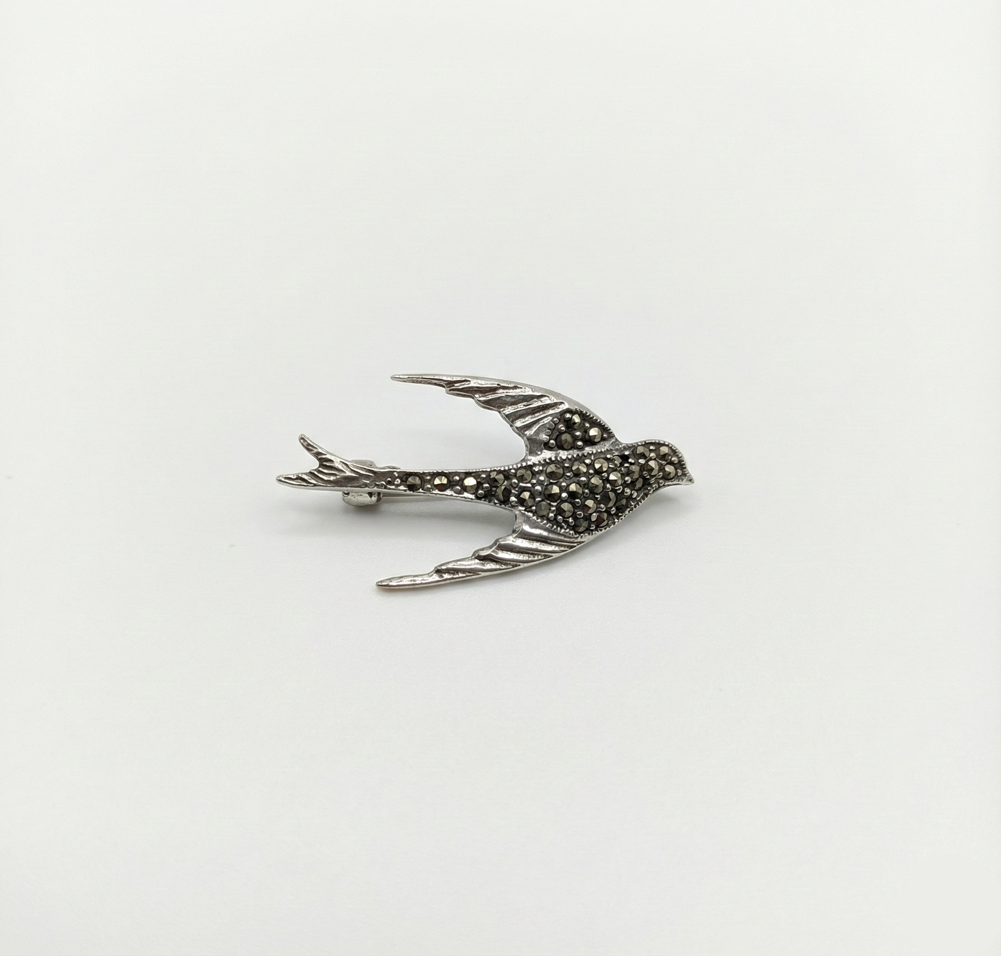 Silver bird-shaped brooch with marcasite stones on a white background