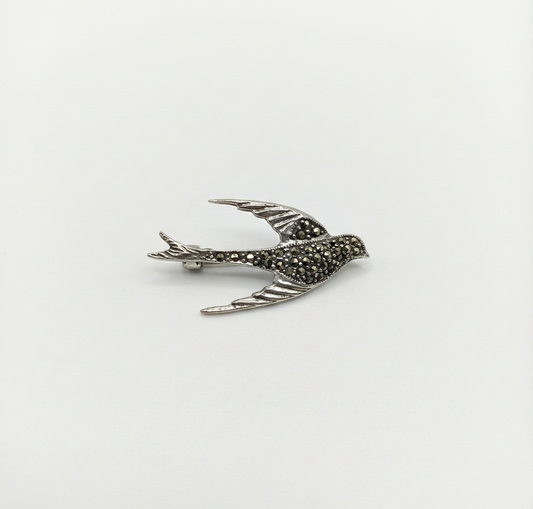 Silver bird-shaped brooch with marcasite stones on a white background