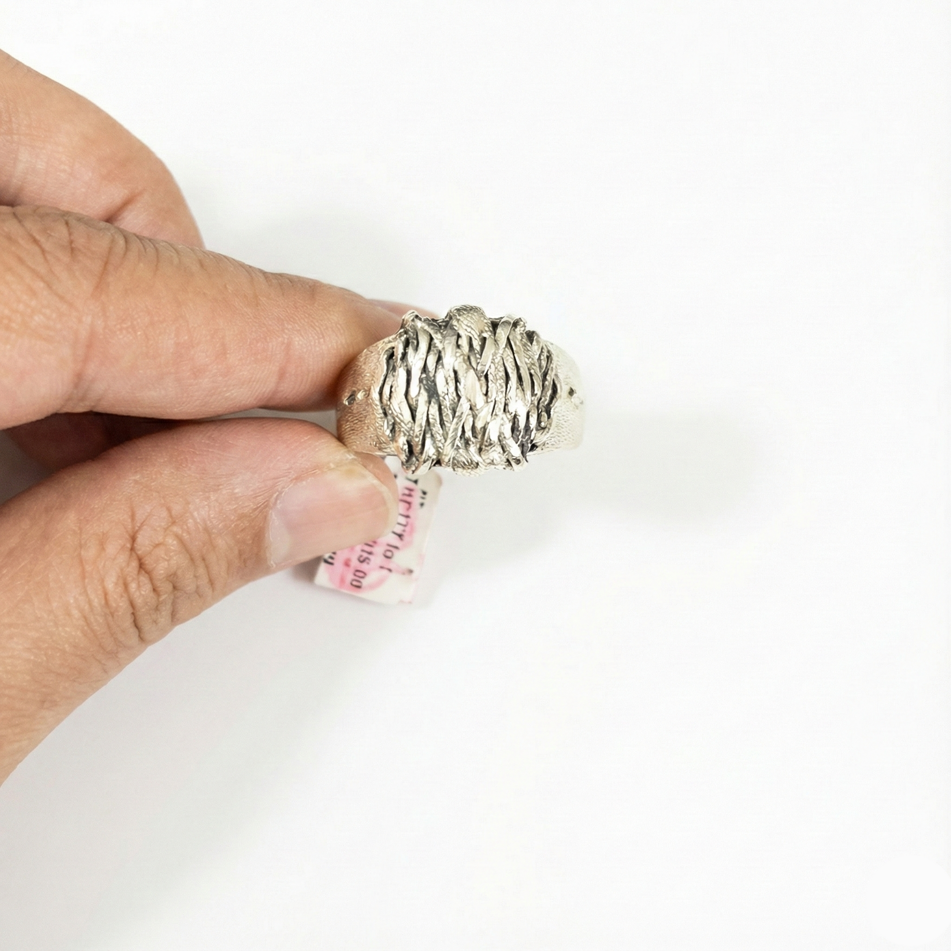 Hand holding a textured silver ring with a white background