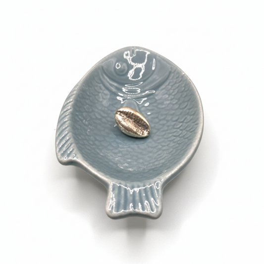 Blue ceramic fish-shaped dish with a small shell on a white background