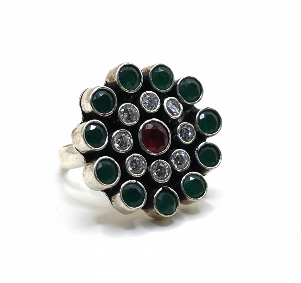 Silver ring with green gemstones and a red gemstone on a white background