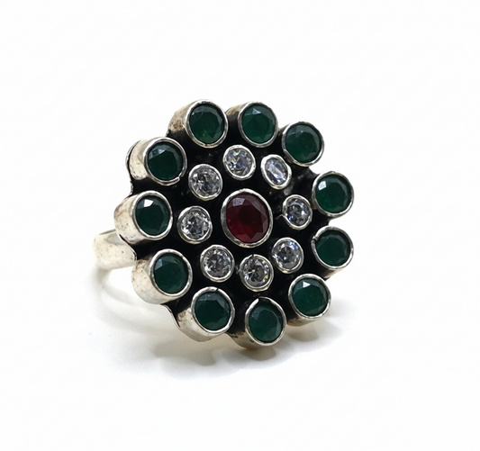 Silver ring with green gemstones and a red gemstone on a white background