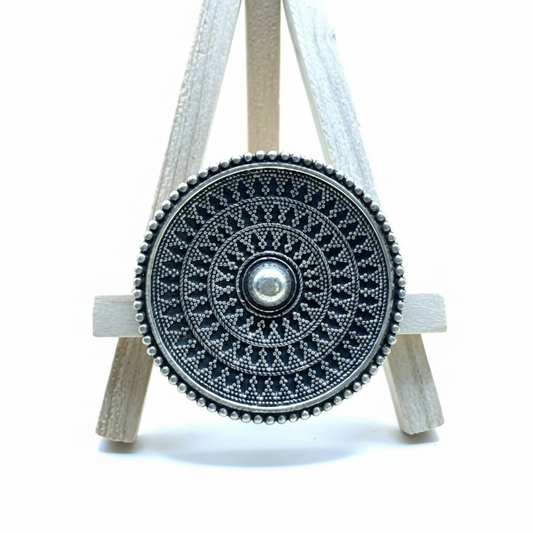 Decorative wheel with intricate patterns on a small wooden stand against a white background
