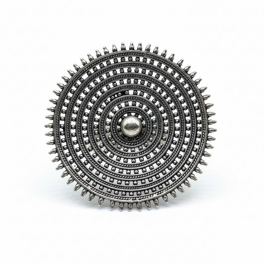 Silver circular brooch with intricate design on a white background