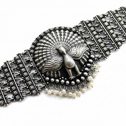 Decorative silver bracelet with peacock design and pearl accents on a white background