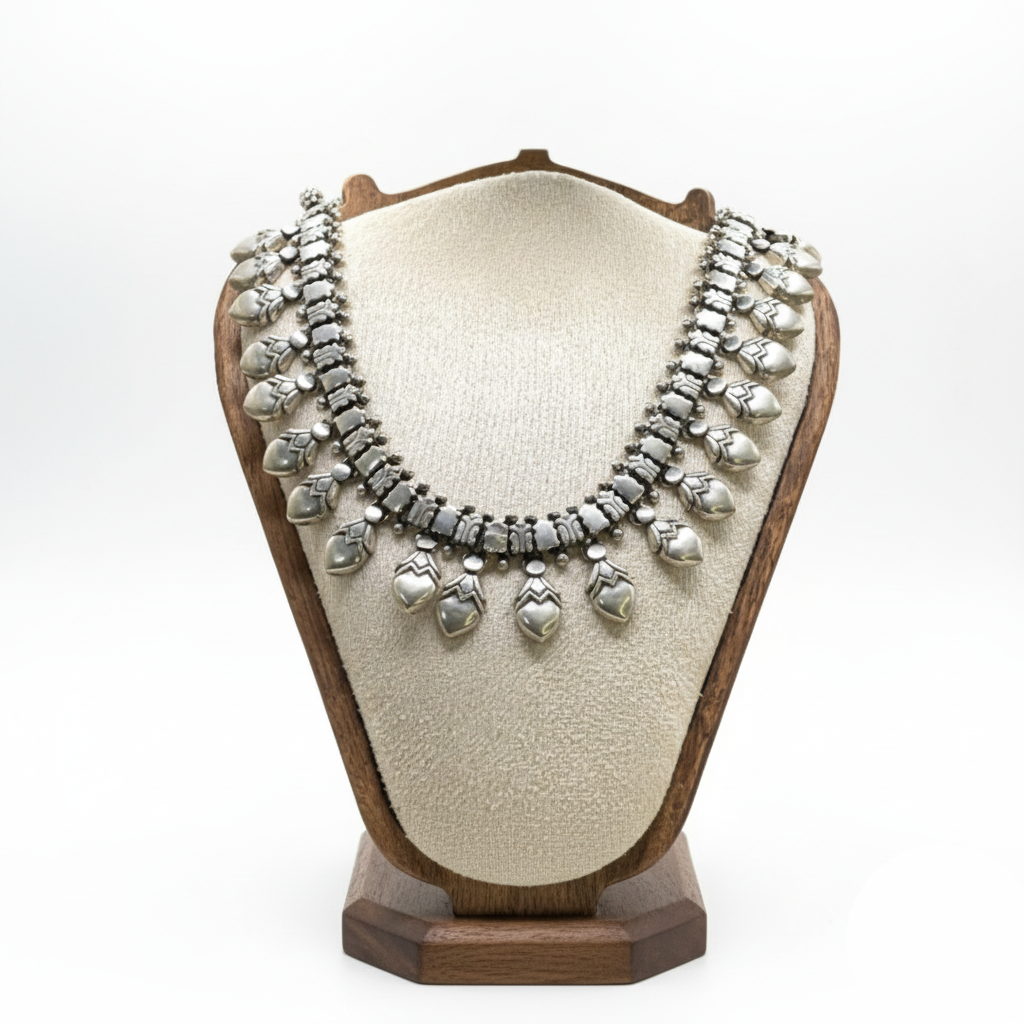 Silver necklace on a wooden and fabric display stand against a white background