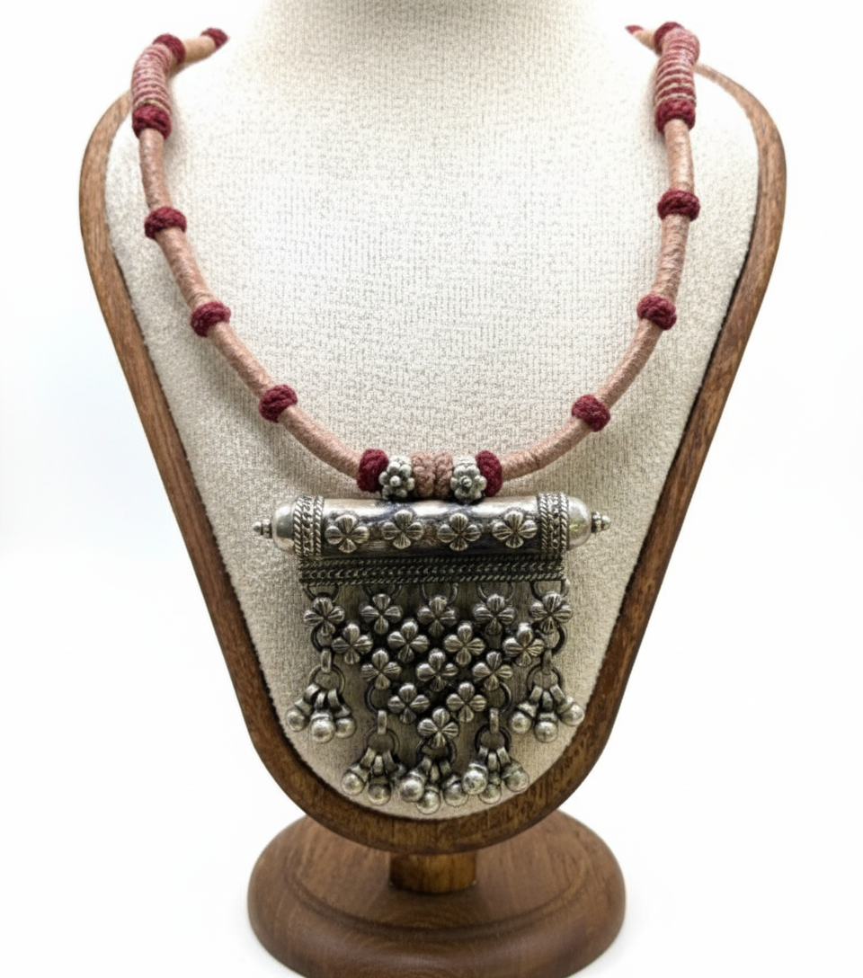 Decorative necklace with silver pendant on a wooden stand against a white background