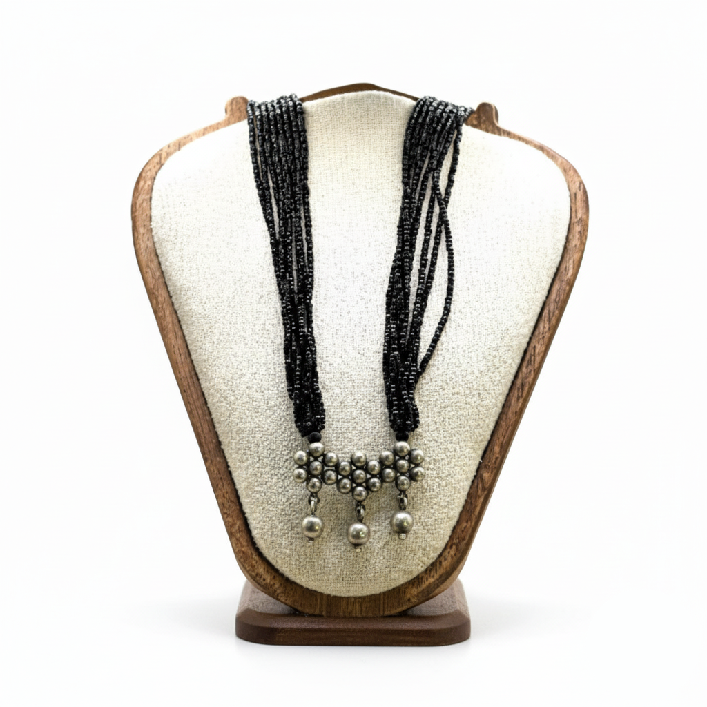 Black beaded necklace with silver pendants on a wooden display stand against a white background