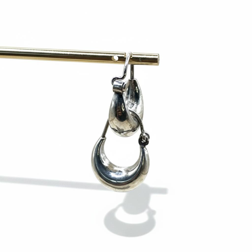 Silver earring hanging from a gold rod on a white background