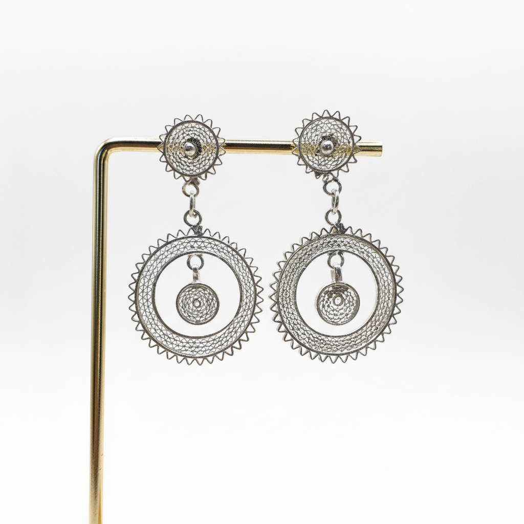 Pair of silver earrings on a gold stand against a white background