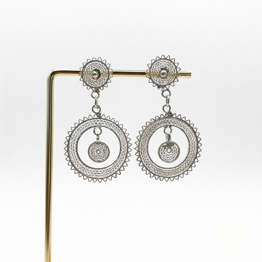 Pair of silver earrings on a gold stand against a white background