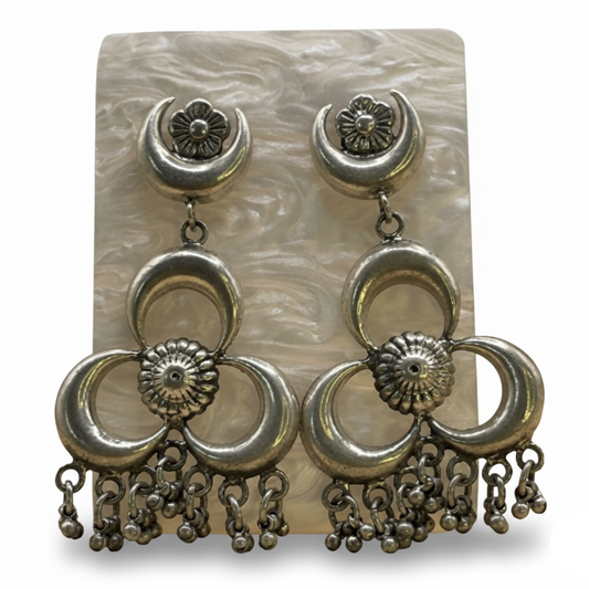 Pair of silver earrings with floral and crescent designs on a textured card.