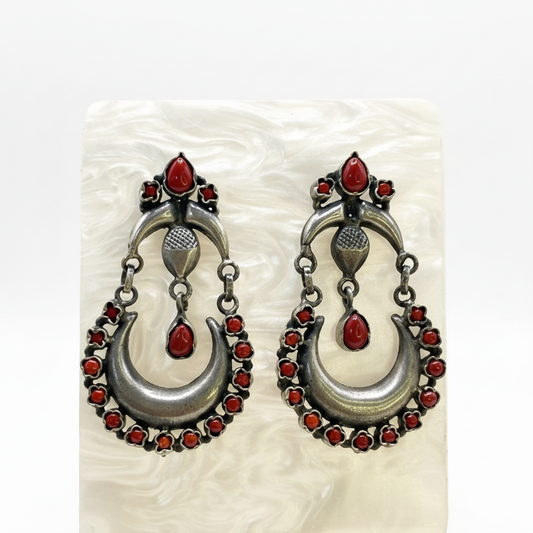Pair of silver earrings with red gemstones on a textured white background
