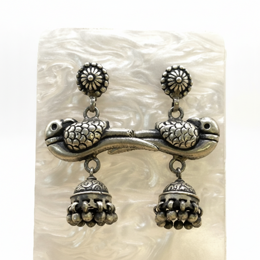 Pair of silver turtle earrings with jhumka designs on a textured white background